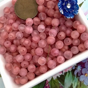 May include: A bowl filled with translucent pink beads. The beads are round and have a frosted finish.