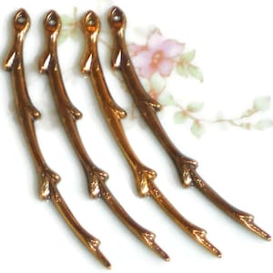 May include: Four gold-toned metal twig-shaped embellishments. Each twig has a slightly different shape and features a small, rounded tip.