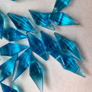 May include: A collection of teal blue crystal-like icicle shaped ornaments. The icicles are made of a clear plastic material and have a faceted design.
