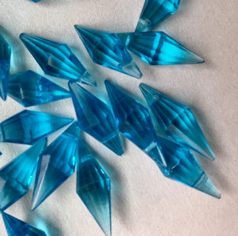 May include: A collection of teal blue crystal-like icicle shaped ornaments. The icicles are made of a clear plastic material and have a faceted design.
