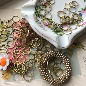 Peut inclure: Un tas d'anneaux de saut dor&eacute;s, certains dans un plat en porcelaine blanche avec des motifs floraux, et une couronne de perles dor&eacute;es sur une carte vintage qui dit "D&eacute;sol&eacute; d'apprendre que vous &ecirc;tes malade".