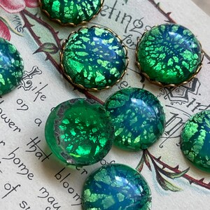 May include: Six green glass cabochons with gold foil accents and brass settings. The cabochons have a mottled, iridescent finish.