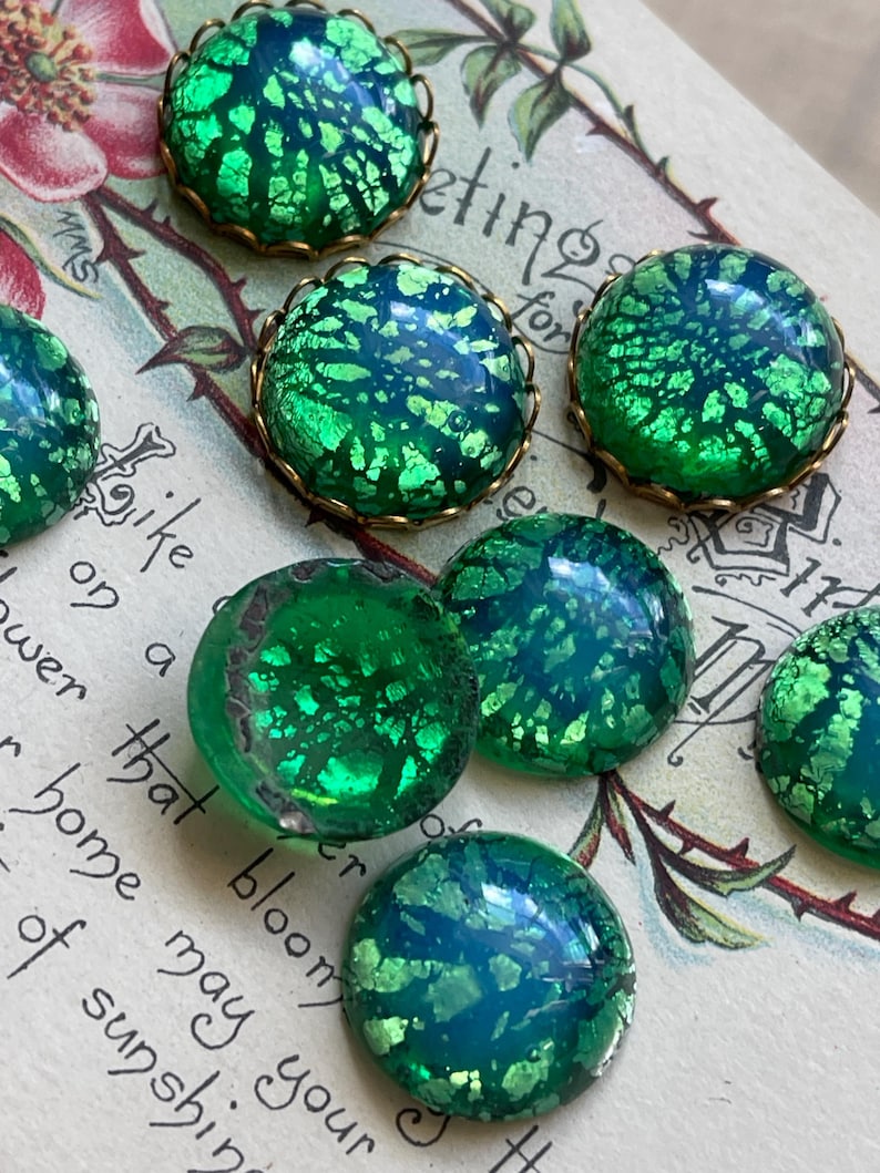 May include: Six green glass cabochons with gold foil accents and brass settings. The cabochons have a mottled, iridescent finish.