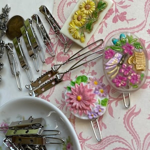 May include: Assortment of silver hair clips with floral-themed ceramic hair clips. The ceramic clips feature pink and white flowers, yellow flowers, and a butterfly with a basket of flowers.
