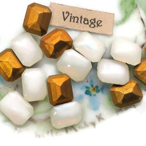May include: A collection of vintage beads in a mix of shapes and colors. Some beads are faceted, metallic gold, while others are smooth, white, and rectangular. A small tag with the word "Vintage" is also present.