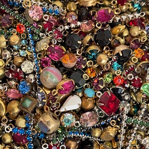 May include: A close-up of a collection of vintage jewellery components. The assortment includes a variety of colourful rhinestones, beads, and metal findings in shades of pink, red, blue, green, and gold. The pieces are of various shapes and sizes.