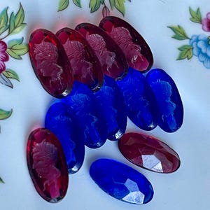 May include: A group of oval-shaped glass beads with a carved design. The beads are in two colors: red and blue.