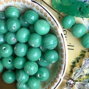 May include: A bowl filled with smooth, green jade beads. The beads have a swirling pattern and are all approximately the same size.