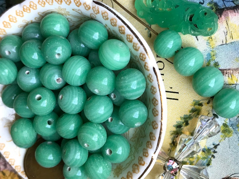 May include: A bowl filled with smooth, green jade beads. The beads have a swirling pattern and are all approximately the same size.
