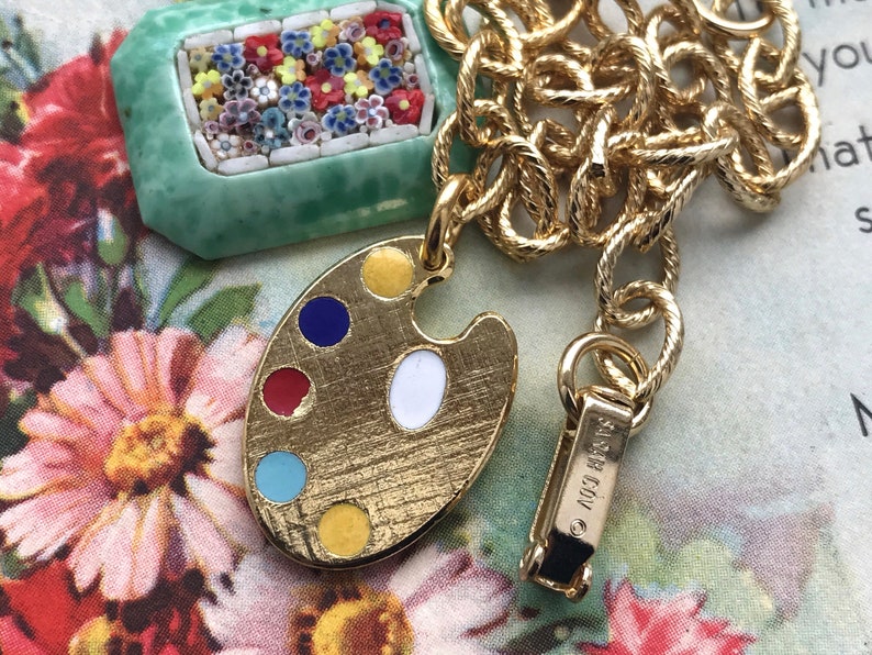 K&ouml;nnte beinhalten: Eine goldene Kettenkette mit einem gr&uuml;nen und wei&szlig;en Mosaik-Anh&auml;nger und einem goldenen Anh&auml;nger in Form einer Malpalette mit buntem Emaille-Anstrich. Die Kette hat einen Verschluss mit der Aufschrift "&copy; 1993 COV."