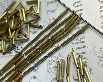 May include: A close-up of a chain made of gold-colored metal tubes. The tubes are connected by small metal rings. The chain is lying on a piece of paper with writing on it.