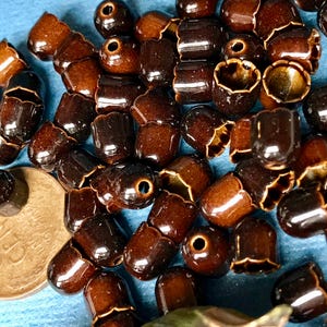 May include: A large group of brown ceramic beads with a shiny glaze. The beads have a scalloped edge and a hole in the center. The beads are scattered on a blue surface.