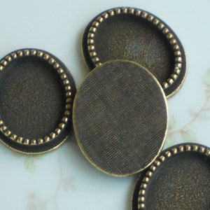 May include: Four round, gold-toned metal tray settings with a beaded edge. The trays are designed to hold small round items, such as cabochons or other decorative elements.