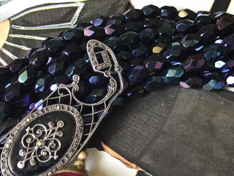 May include: A silver filigree pendant with a black oval cameo and a row of iridescent black beads.