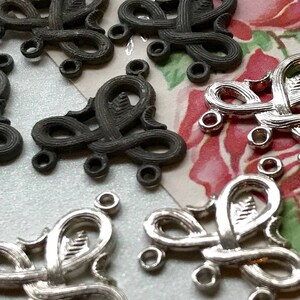 May include: A close-up of silver and black metal decorative embellishments with intricate designs. The embellishments have multiple loops and are shaped like hearts.