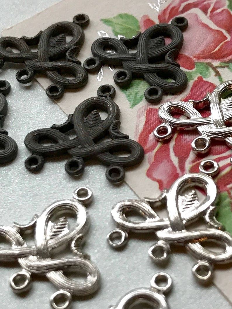 May include: A close-up of silver and black metal decorative embellishments with intricate designs. The embellishments have multiple loops and are shaped like hearts.