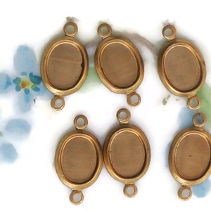 May include: Six gold-toned oval-shaped metal pendant trays with a smooth surface and three loops on each side.