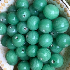 May include: A bowl filled with smooth, round, green jade beads. The beads have a subtle swirl pattern and a hole in the center.