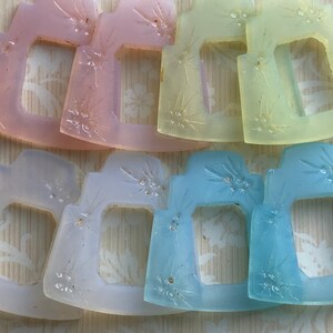 May include: Six pastel-colored glass frames with a starburst design. The frames are in shades of pink, yellow, blue, and white.