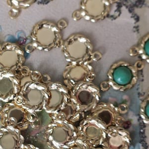 May include: A close-up of gold-toned metal connector charms with a rope-like design. Some charms have a round, flat center, while others have a green gemstone in the center.