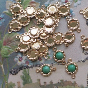 May include: A group of gold-toned metal settings with a rope-like design. Each setting has two loops for attaching to a chain or cord. Some settings have a green glass cabochon in the centre.