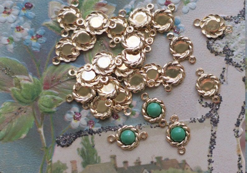May include: A group of gold-toned metal settings with a rope-like design. Each setting has two loops for attaching to a chain or cord. Some settings have a green glass cabochon in the centre.