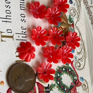 May include: A collection of ten red plastic flower-shaped buttons. The buttons are approximately the size of a US penny.