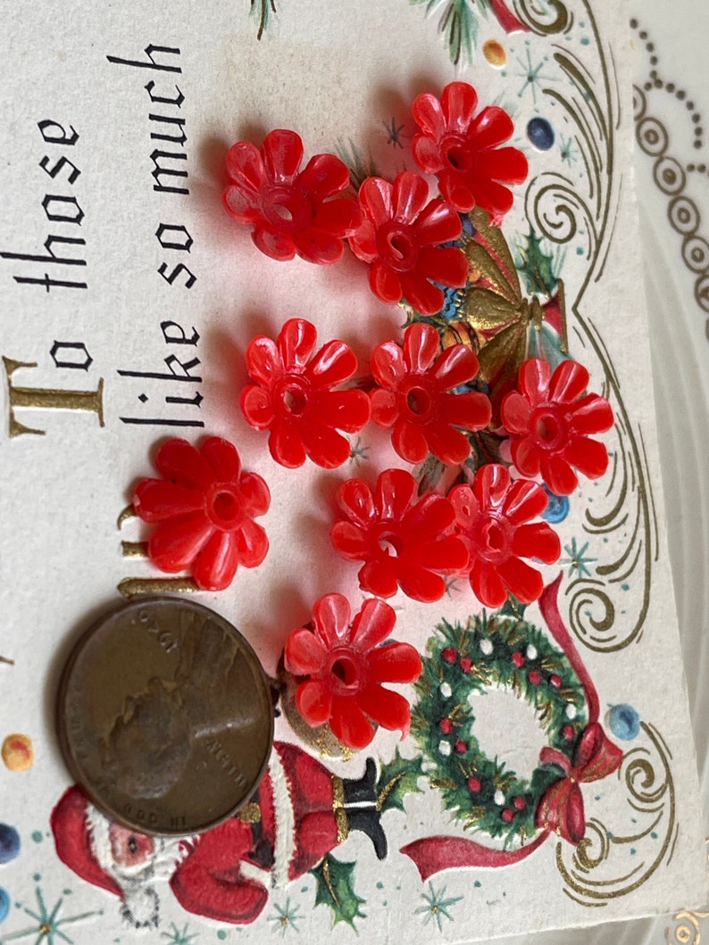 May include: A collection of ten red plastic flower-shaped buttons. The buttons are approximately the size of a US penny.