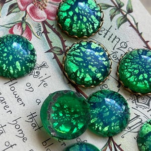 May include: Assortment of green iridescent glass cabochons with gold foil accents. The cabochons are set in gold-toned metal bezels with scalloped edges.