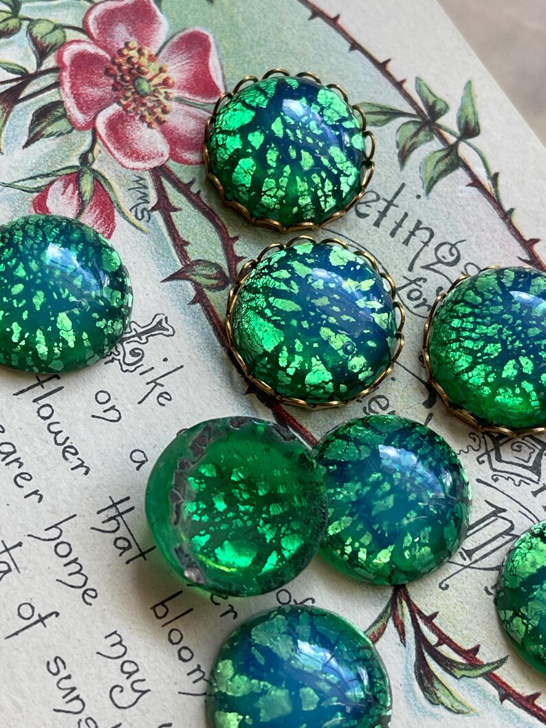 May include: Assortment of green iridescent glass cabochons with gold foil accents. The cabochons are set in gold-toned metal bezels with scalloped edges.