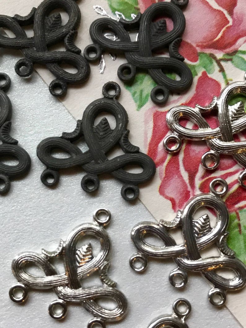 May include: A close-up of eight metal decorative pieces. Four are silver and four are black. Each piece is shaped like a stylized heart with three loops at the bottom. The pieces are arranged in a random pattern.