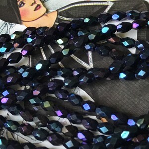May include: A strand of iridescent black faceted glass beads. The beads are oval shaped and have a dark blue, purple, and green iridescent sheen.