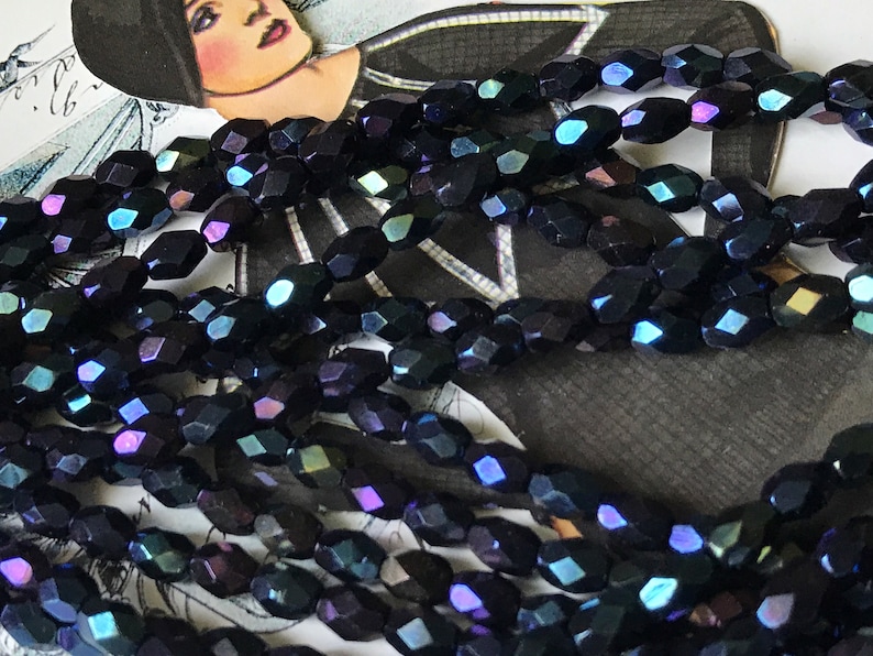 May include: A strand of iridescent black faceted glass beads. The beads are oval shaped and have a dark blue, purple, and green iridescent sheen.