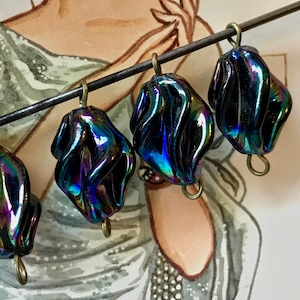 May include: Four iridescent black glass beads with a swirl design and silver metal loops. The beads are strung on a wire.