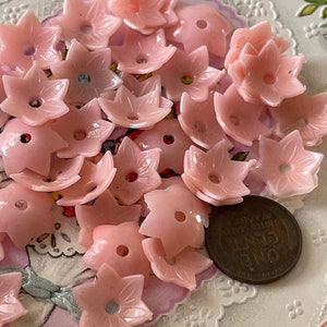 Peut inclure: Un ensemble de boutons en plastique rose en forme de fleur. Les boutons ont cinq pointes et un trou au centre. Il y a une pi&egrave;ce de monnaie d'un penny dans l'image pour l'&eacute;chelle.