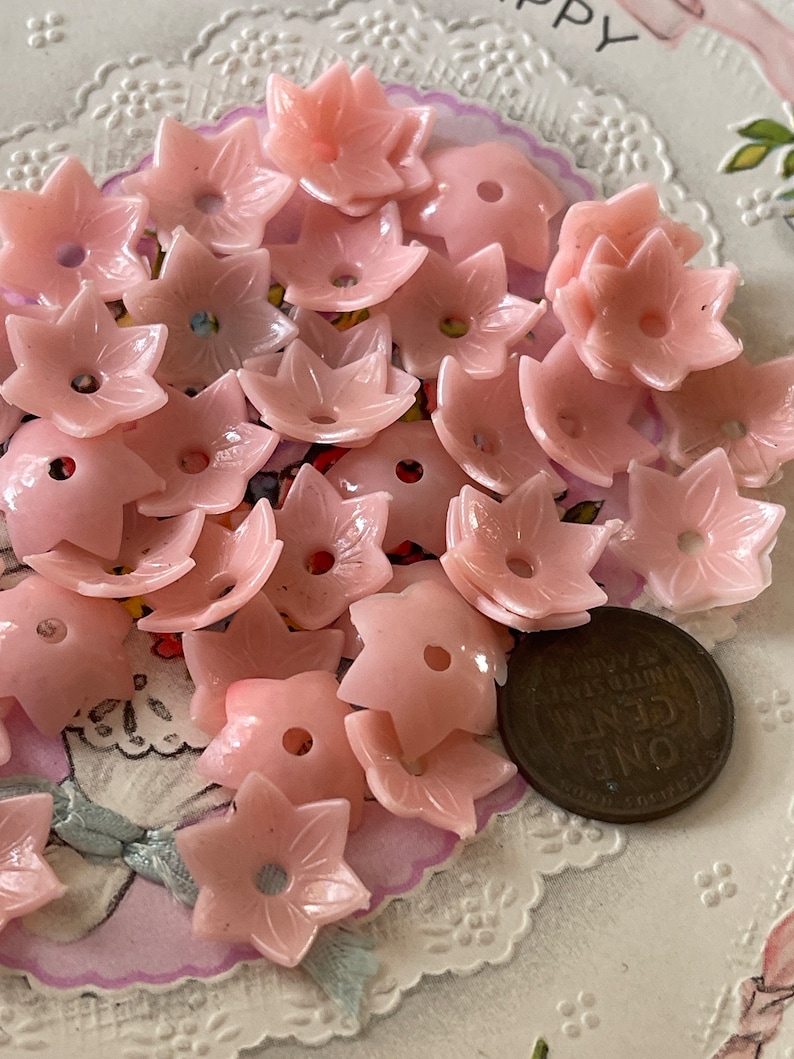 Peut inclure: Un ensemble de boutons en plastique rose en forme de fleur. Les boutons ont cinq pointes et un trou au centre. Il y a une pi&egrave;ce de monnaie d'un penny dans l'image pour l'&eacute;chelle.