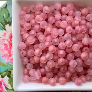 May include: A bowl filled with translucent pink beads. The beads are round and have a frosted finish.