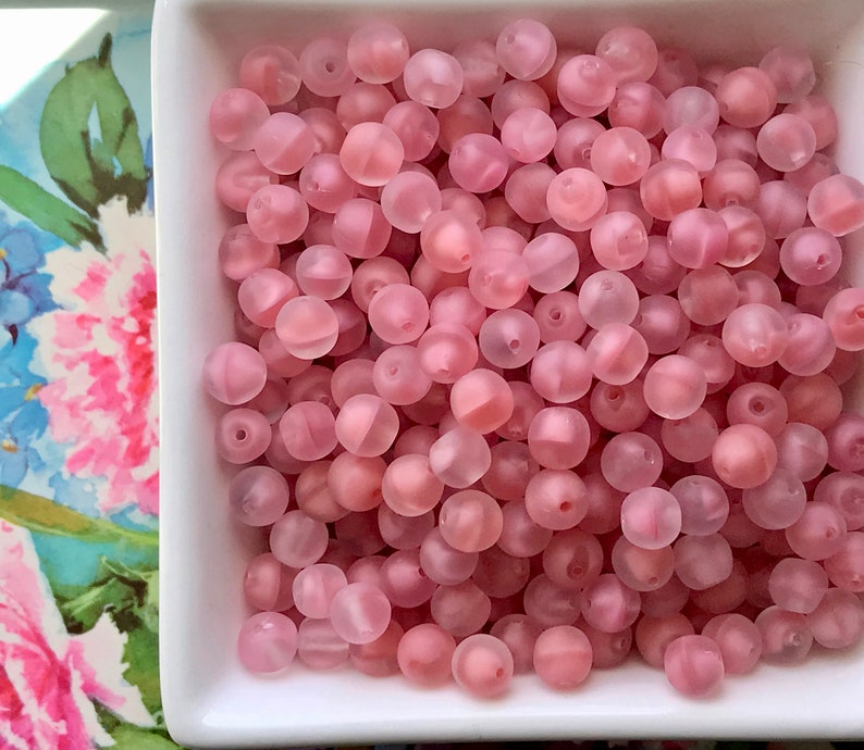 May include: A bowl filled with translucent pink beads. The beads are round and have a frosted finish.