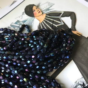 May include: A strand of iridescent dark blue glass beads. The beads are faceted and have a slightly oval shape.