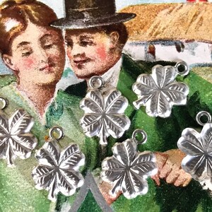 May include: Seven silver four-leaf clover charms with a textured surface. The charms have a loop at the top for attaching to a necklace or bracelet.