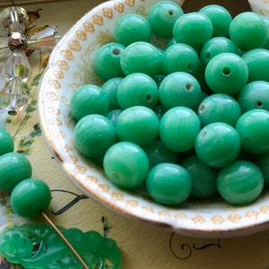 May include: A bowl filled with smooth, green jade beads. The beads are round and have a subtle swirl pattern.