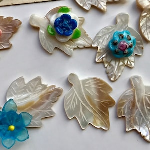 May include: Assortment of white mother of pearl leaves with various colored glass flower embellishments. The flowers are blue, pink, and turquoise.