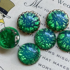 May include: Five green glass buttons with gold foil accents and a brass rim. The buttons have a mottled, iridescent finish.