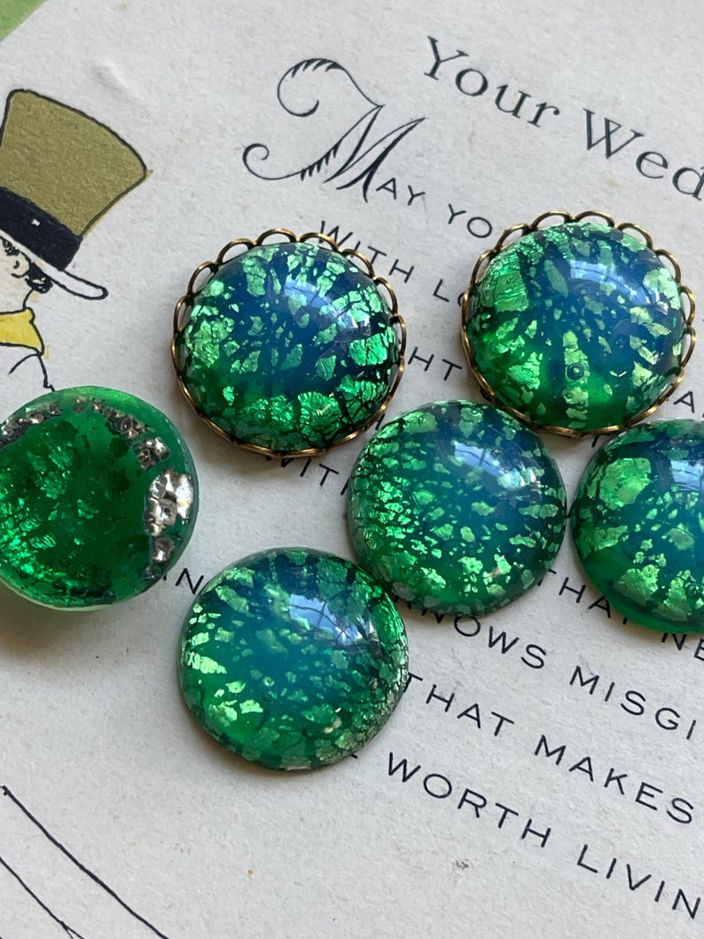 May include: Five green glass buttons with gold foil accents and a brass rim. The buttons have a mottled, iridescent finish.