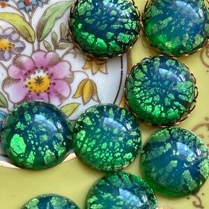 May include: A collection of eight green iridescent glass cabochons with gold settings. The cabochons have a speckled, crackled appearance.