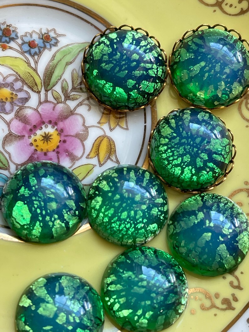 May include: A collection of eight green iridescent glass cabochons with gold settings. The cabochons have a speckled, crackled appearance.