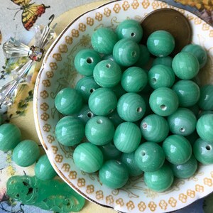 May include: A bowl of green jade beads. The beads are round and have a smooth, polished finish. They are perfect for making jewelry or other crafts.