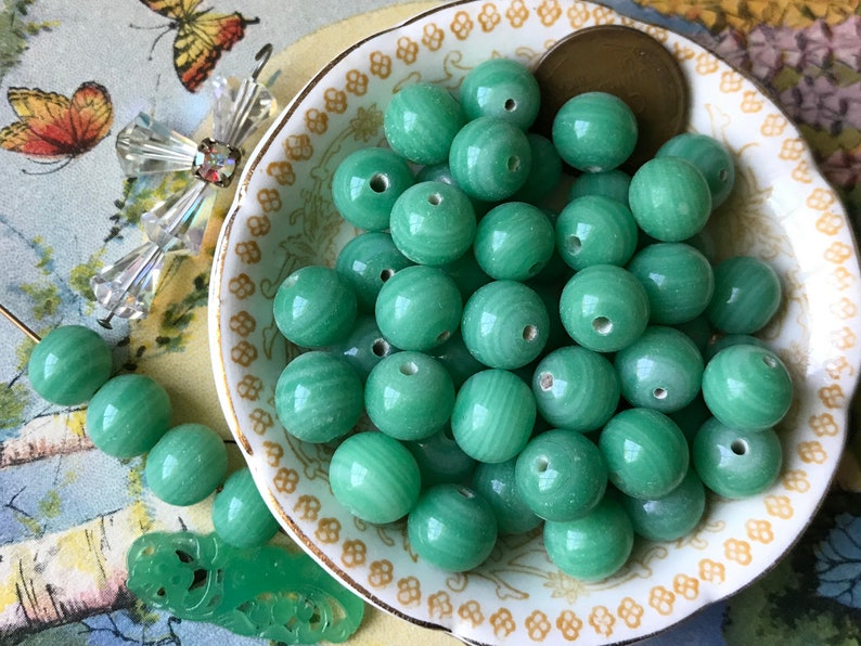May include: A bowl of green jade beads. The beads are round and have a smooth, polished finish. They are perfect for making jewelry or other crafts.