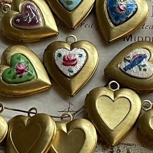 May include: A collection of ten gold heart-shaped locket pendants with various enamel designs. Some of the designs include floral patterns, birds, and geometric shapes.