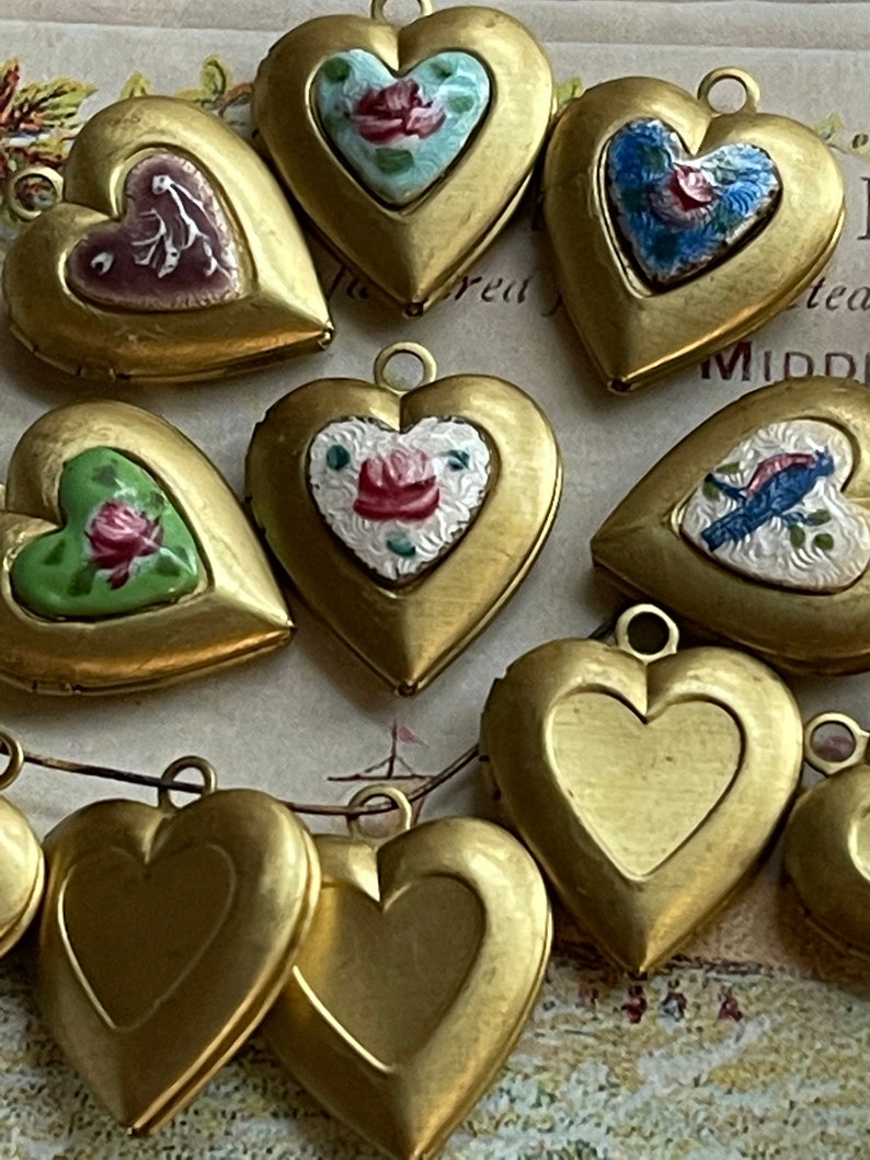 May include: A collection of ten gold heart-shaped locket pendants with various enamel designs. Some of the designs include floral patterns, birds, and geometric shapes.